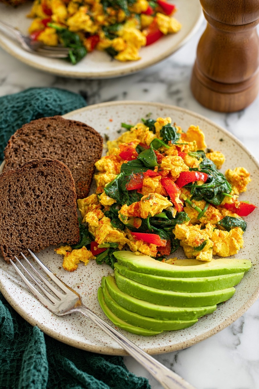 Vegan Tofu Scramble Spinach, plant-based breakfast recipes, healthy vegan breakfast, quick vegan scramble, protein-packed tofu breakfast - A white plate filled with three layers of food: the bottom layer is cooked yellow tofu pieces with some green bits mixed in, the middle layer has bright red bell pepper pieces scattered, and the top layer is fresh dark green spinach leaves spread evenly. To the left of the plate, there is a silver spoon resting on the edge, and below that, a small wooden bowl contains six thin slices of light green avocado stacked neatly. In the background, three slices of bread with different brown shades are placed on the white marbled surface near the plate. A green cloth napkin is on the lower right side of the plate. Photo taken with an iphone --ar 2:3 --v 7