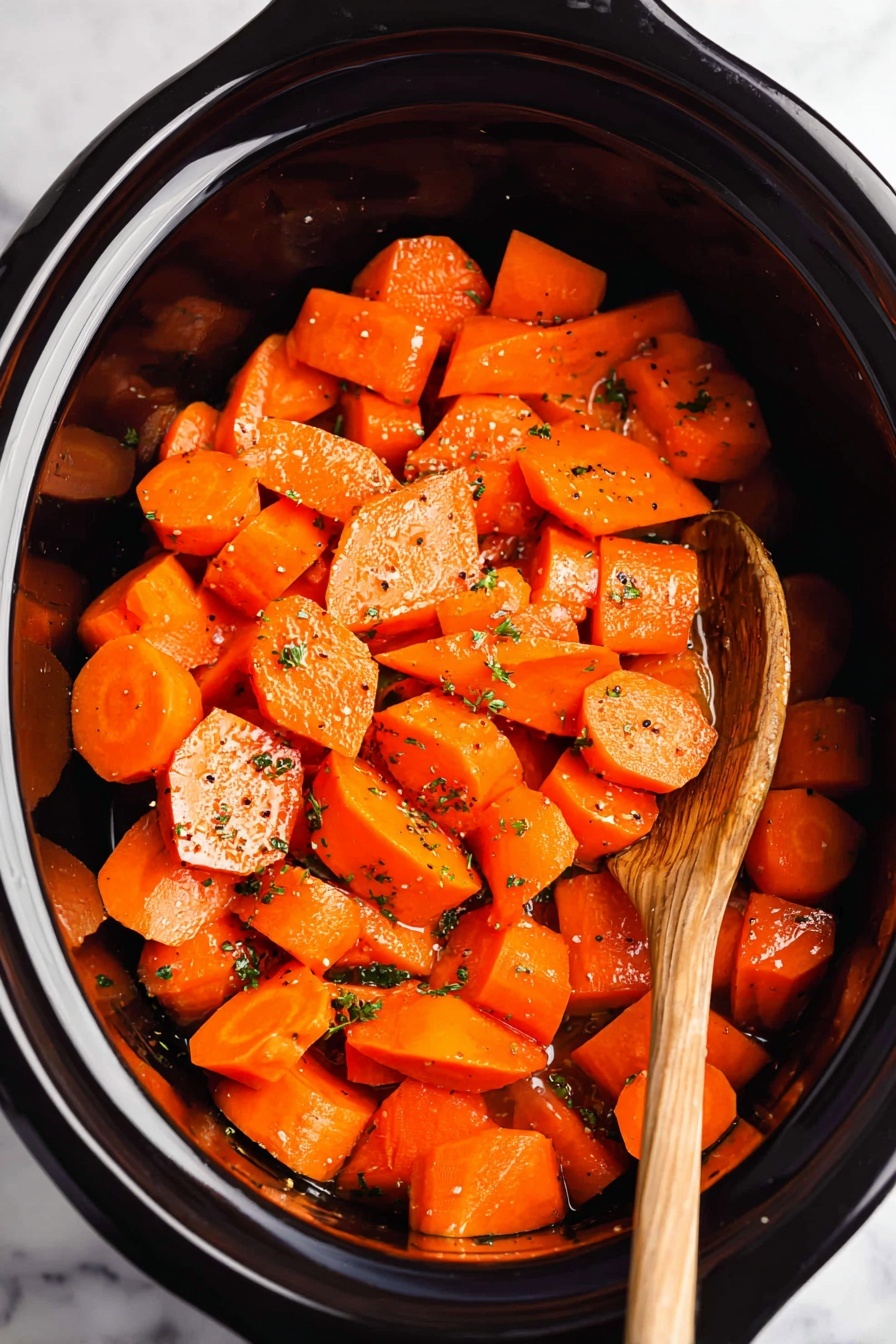 Sweet Honey Garlic Crockpot Carrots, honey garlic carrots, slow cooker carrot side dish, easy healthy carrot recipes, tender glazed carrots - The image shows a close-up of chunky bright orange carrot pieces, cut into irregular shapes including thick rounds and triangular chunks, all coated with a shiny glaze. Small bits of fresh green herbs and scattered black pepper flakes are sprinkled on top, adding texture and color contrast. The carrot pieces fill the frame densely, with a wooden spoon partially visible, stirring the carrots from the bottom right corner. The background is a white marbled texture. photo taken with an iphone --ar 2:3 --v 7