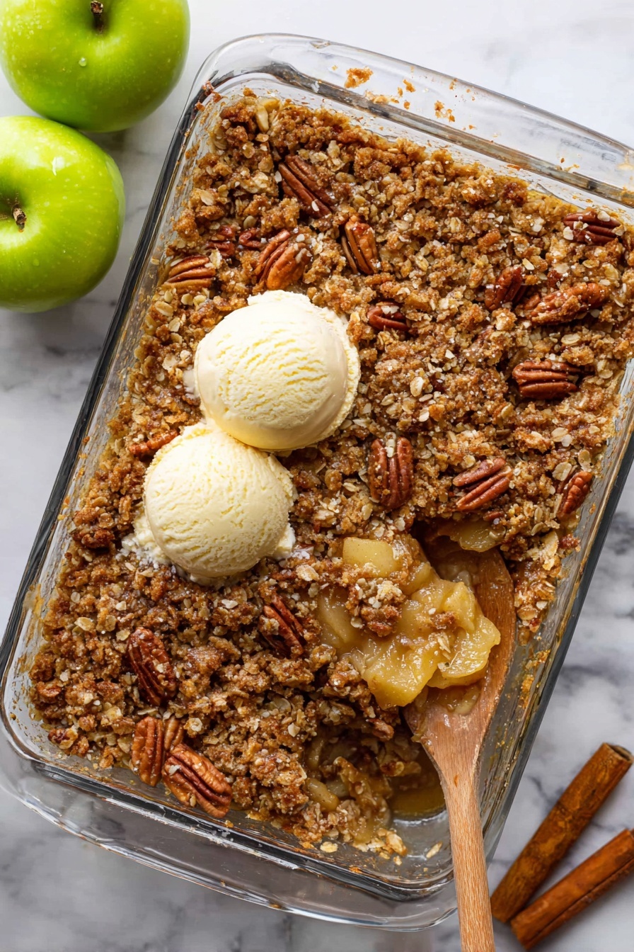 Apple Pecan Crisp, apple pecan crisp, easy apple dessert, fall dessert recipes, crunchy apple crumble - A clear glass baking dish filled with a golden brown apple crisp topped with a crunchy layer of chopped pecans and oats, showing a slightly uneven texture with bits of the crumble mix. Two creamy, round scoops of vanilla ice cream sit near the center on top of the dessert. A wooden spoon inside the dish scoops out a portion, revealing a moist, soft apple layer underneath with a light, yellowish color. The background is a white marbled surface with two green apples on the left and a cinnamon stick on the right. Photo taken with an iphone --ar 2:3 --v 7
