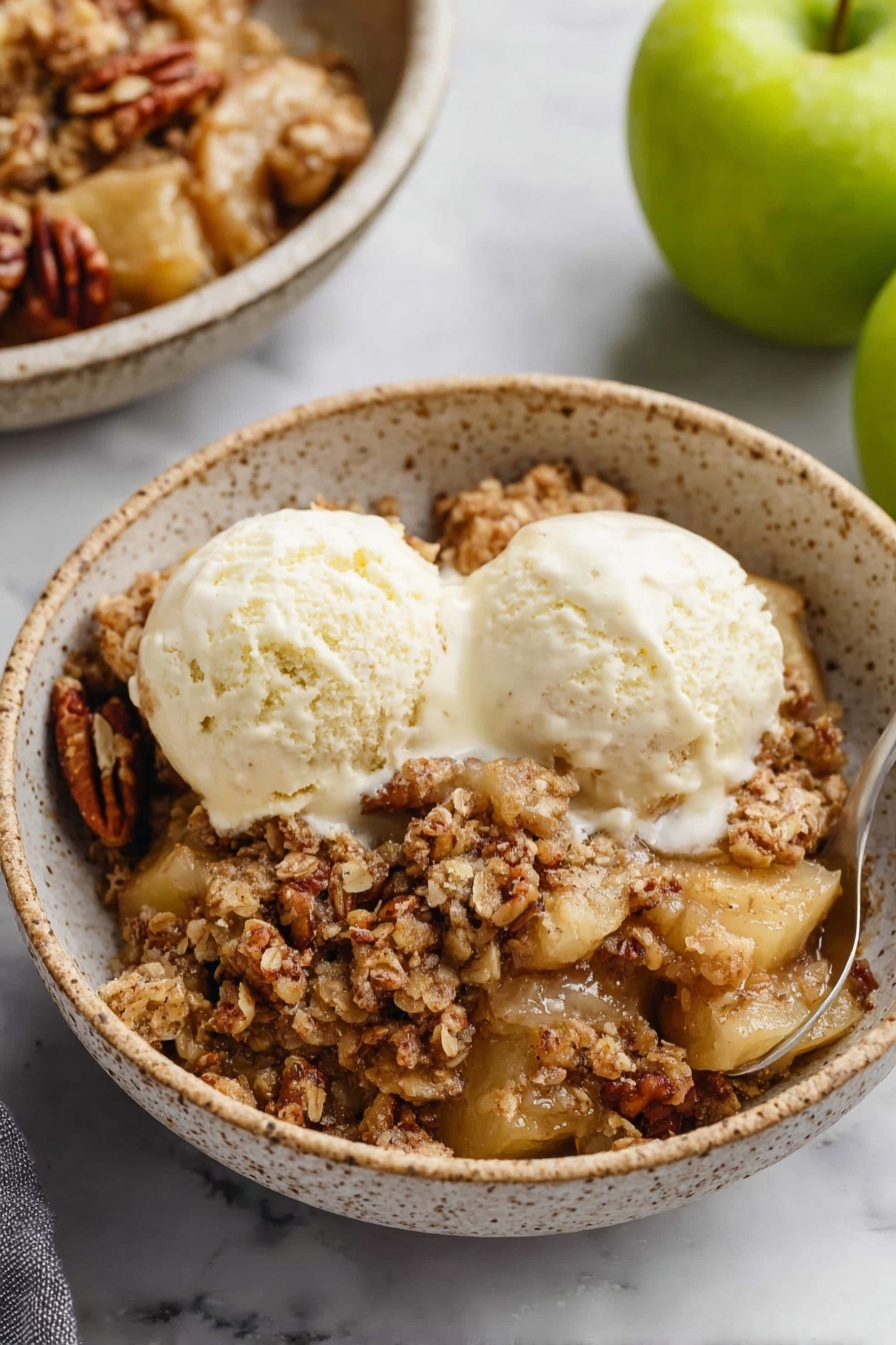 Apple Pecan Crisp, apple pecan crisp, easy apple dessert, fall dessert recipes, crunchy apple crumble - A white bowl filled with a warm apple crumble dessert, showing a bottom layer of soft, cooked apple pieces that are light golden brown, covered by a chunky crumb topping made of oats and chopped nuts in a brown, crumbly texture. On top, two round scoops of creamy vanilla ice cream sit slightly melting over the crumble. A silver spoon is placed inside the bowl, digging into the dessert, with its handle resting on the edge. The background is a white marbled surface, with two cinnamon sticks placed nearby, and a gray cloth partially visible on the side. Photo taken with an iphone --ar 2:3 --v 7