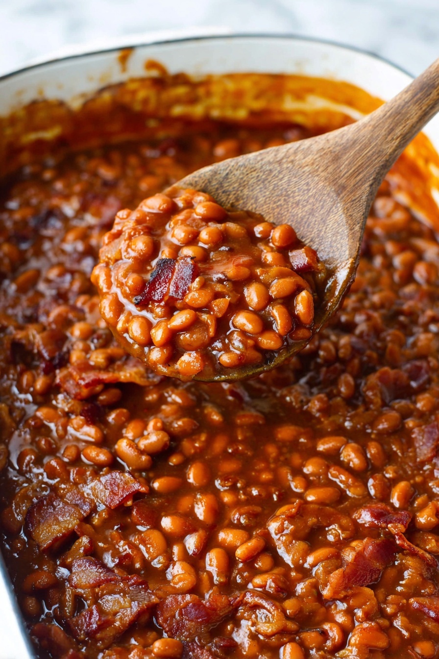Best Baked Beans, baked beans recipe, smoky baked beans, hearty side dishes, easy baked beans - A close-up of a white rectangular baking dish filled with baked beans in a thick, shiny dark reddish-brown sauce. The beans are soft and mixed with small pieces of cooked bacon that have a crispy texture and a light to dark brown color. A dark wooden spoon is resting on the right side, scooping some beans and bacon, showing the chunky texture with a glossy sauce coating. The edges of the dish have small sauce splatters, and the background is a white marbled surface. photo taken with an iphone --ar 2:3 --v 7