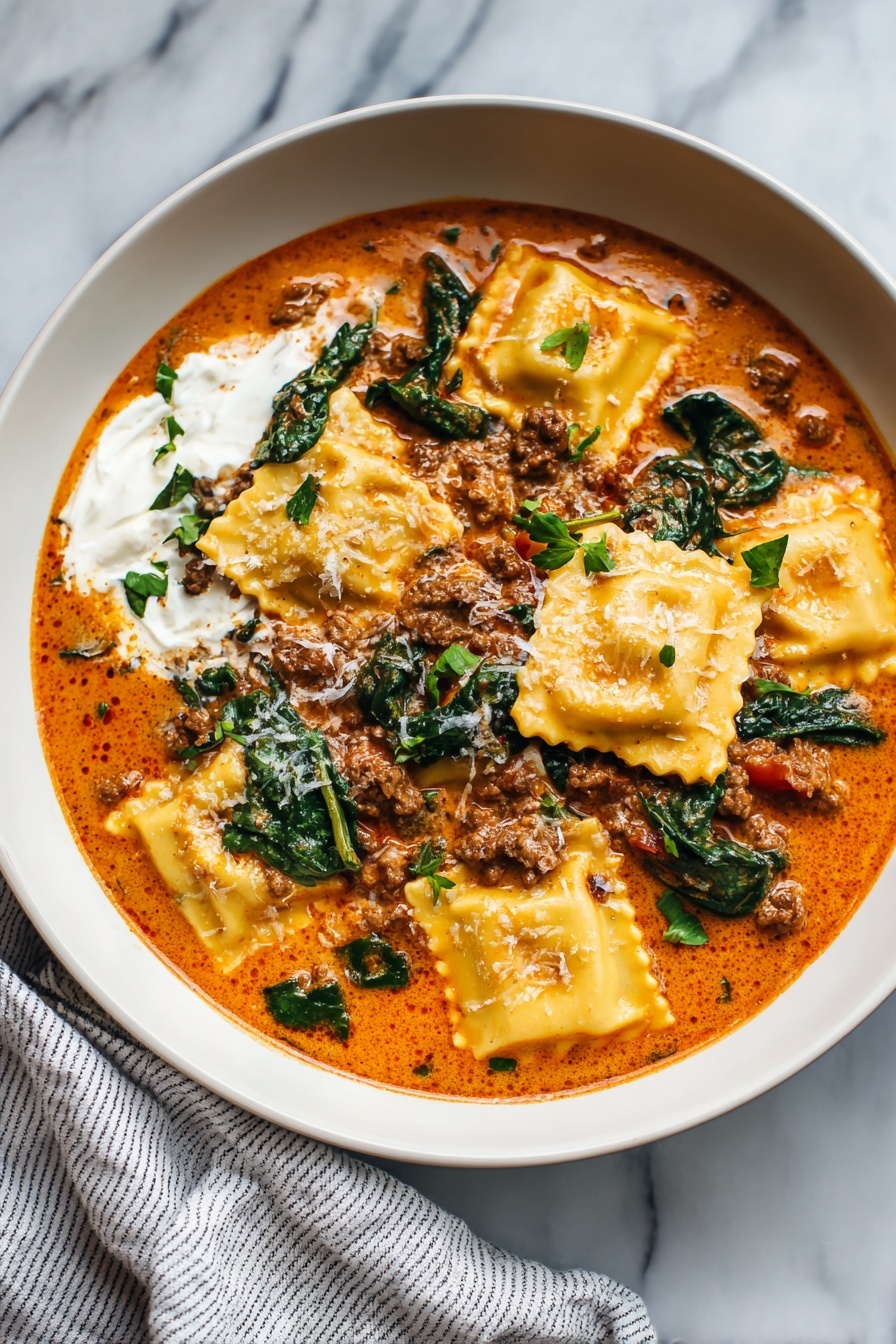 Cheesy Ravioli Soup with Spinach, Italian ravioli soup, easy cheesy ravioli soup, comfort food ravioli recipe, quick spinach ravioli soup - A white bowl with a creamy orange sauce filled with several pieces of ravioli, some cooked spinach leaves, and small chunks of ground meat scattered on top, sprinkled lightly with black pepper. A generous dollop of white cream sits on one side of the dish. A silver spoon rests inside the bowl, slightly submerged in the sauce. The bowl is placed on a white marbled surface. Photo taken with an iphone --ar 2:3 --v 7